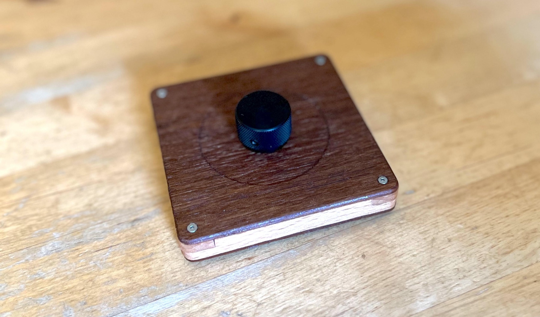 TrigOne Mini wooden MIDI controller with a black rotary encoder on a workbench